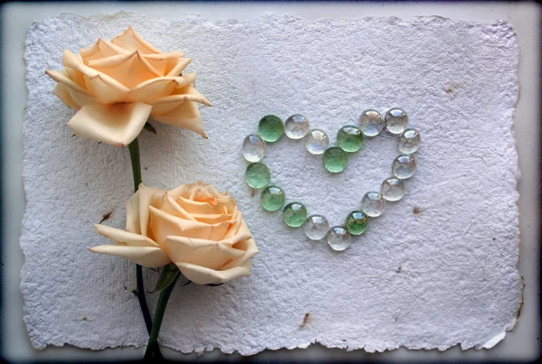 Grunge duas belas rosas amarelas Fundo com um coração de contas de vidro — Fotografia de Stock