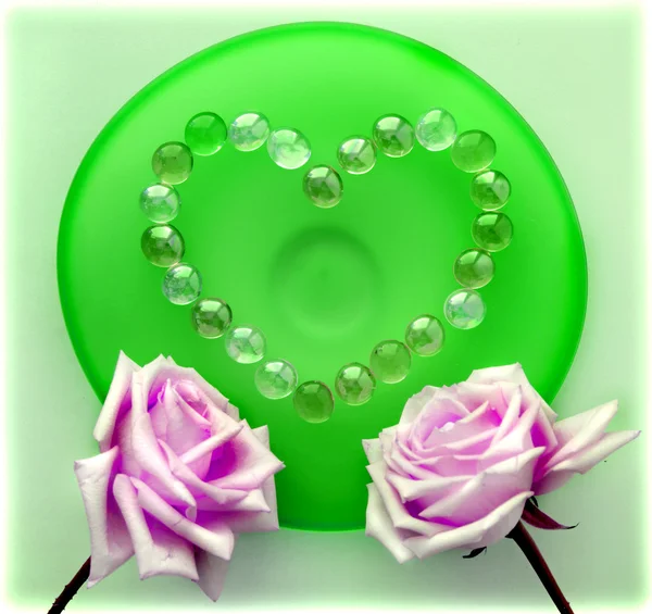 Dos rosas rosadas con un corazón de cuentas de vidrio en placa de vidrio verde —  Fotos de Stock