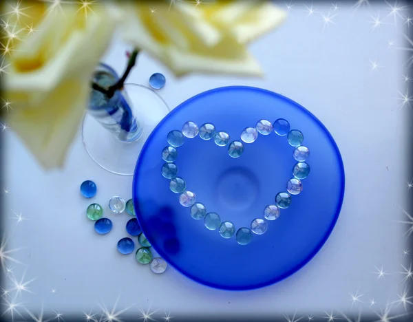 Two white roses with a heart from glass beads on blue glass plate