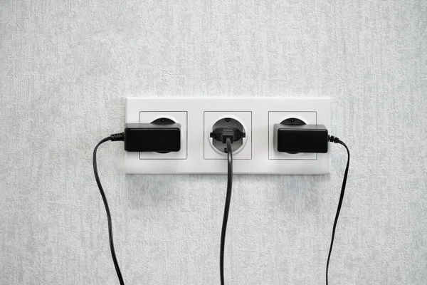 Power European electric plug  on a white. black electric cord plugged into a white electricity socket on white background