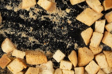 Siyah arka planda pişmiş krakerler. Yakın plan. Kurutulmuş küçük ekmek parçaları. Ekmek kırıntıları.