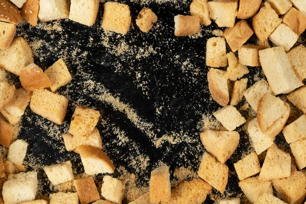 Siyah arka planda pişmiş krakerler. Yakın plan. Kurutulmuş küçük ekmek parçaları. Ekmek kırıntıları.