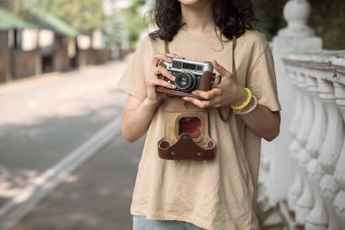 Caddenin arka tarafında elinde eski model kamera olan bir kadın.