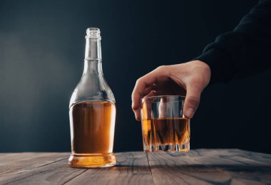 Elinde bardak ve içki şişesi tutan adam.