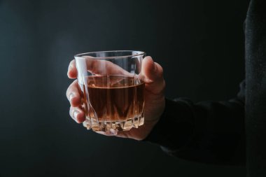 Karanlık sırtüstü uzanmış elinde bir bardak alkol tutan adam.