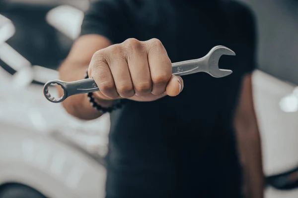 Hand holding a wrench with a car repairs, professional auto mechani