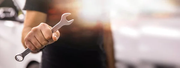 Hand holding a wrench with a car repairs, professional auto mechani