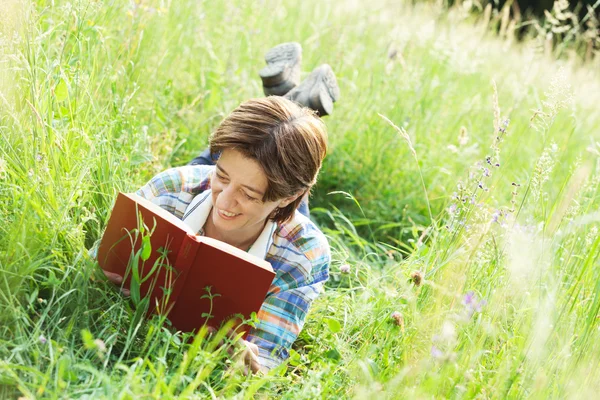 背の高い草で横になっている本を読んでいる女の子 — ストック写真