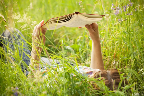 背の高い草で横になっている本を読んでいる女の子 — ストック写真