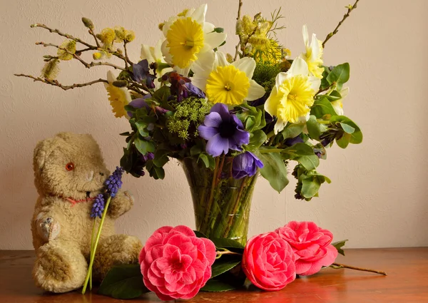 Ein ramponierter alter Teddybär neben Frühlingsblumen — Stockfoto