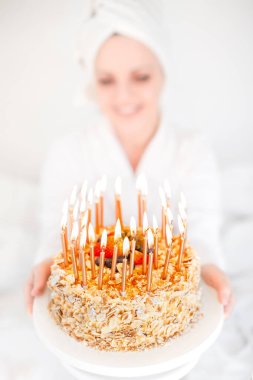 Banyo havlusu ve üzerinde doğum günü pastası olan bir kızın bulanık portresi mumlarla yakın plan. Sabahın erken saatlerinde doğum günü kutlaması. Duştan sonra. Haus