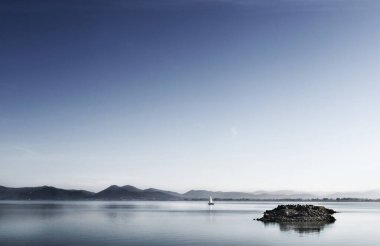 Trasimeno Gölü 'nün sakin sularında bir yelkenli, İtalya' da, ön plandaki kayalıklarda su üzerinde.