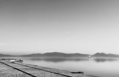 Trasimeno Gölü 'nün sakin sularında bir yelkenli, İtalya' nın ön kıyılarında küçük kasabalar, siyah ve beyaz fotoğrafçılık.