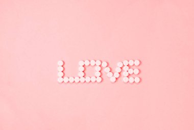 Tek kelimelik aşk pembe arka planda beyaz haplarla yapılır., 