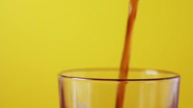 Kahverengi içeceği sarı arkaplanda cama döküyorum.