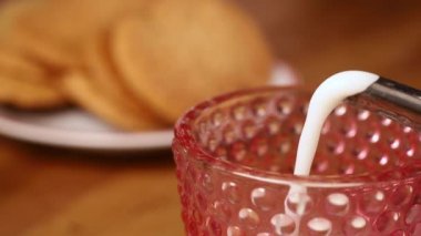 Pembe bardağa süt dökerek, arka plandaki kurabiyelere...