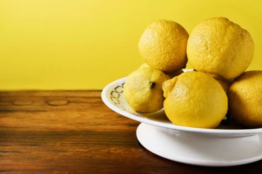 Tahta masada beyaz tabakta olgun limonlar, sağlıklı yiyecekler. 