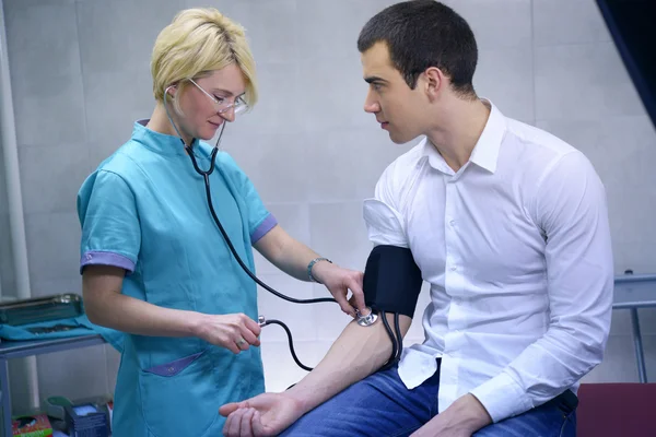 Medico femminile che controlla la pressione sanguigna del giovane uomo — Foto Stock