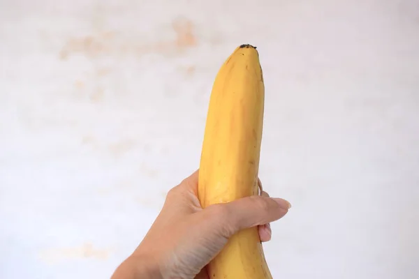 Ripe banana in female hand on light background.