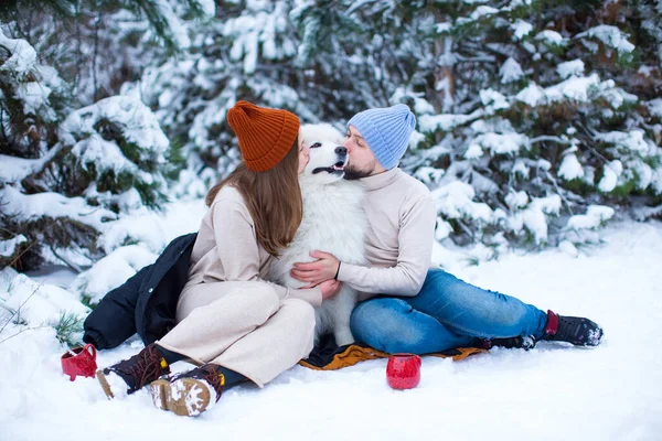 Genç bir çift - bir adam ve güzel bir köpeği olan bir kız - Samoyed karlı bir ormanda çay içer. Mutlu yıllar ve mutlu Noeller.