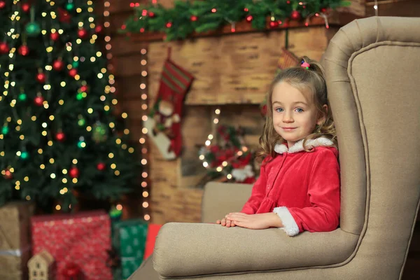 身穿红衣服的漂亮小女孩坐在椅子上 靠着圣诞树和壁炉庆祝圣诞节 — 图库照片