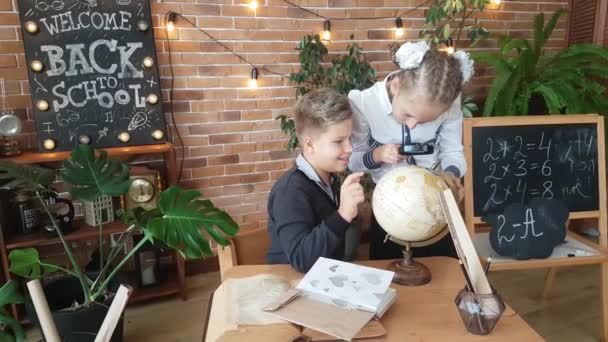 学生们 一个男孩和一个女孩在教室里拿着放大镜 靠着砖墙 带着花环和鲜花 正在全球范围内进行研究 欢迎回到学校 — 图库视频影像