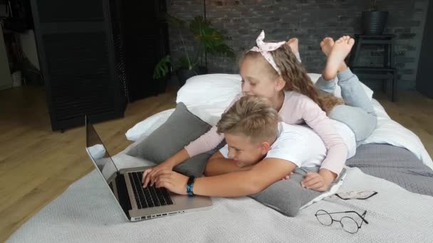 女の子と家の服の男の子はベッドの上にあり ラップトップで抱き合って遊んでいます — ストック動画