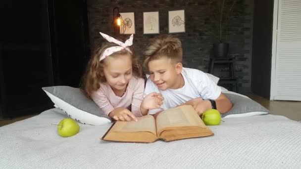 Діти Хлопчик Дівчинка Лежать Ліжку Великою Енциклопедією Яблуками Читають Розмовляють — стокове відео