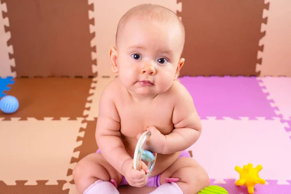 A newborn baby is holding a favorite toy in the playroom. Soft, safe floor covering