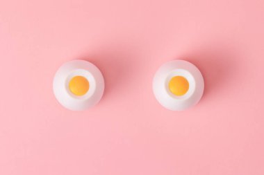 Pembe arka planda iki beyaz-sarı nesne dişi göğsünü sembolize ediyor. Düz yatıyordu. Uzayı kopyala Meme Kanseri Farkındalığı Ayı.