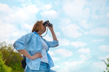 Dürbünle bakan bir kadın turist. Arka planda bulutlu mavi bir gökyüzü. Alt görünüm.