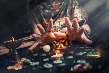 Astroloji ve ezoterizm. Mum ve rün taşlarındaki cadı. Havada ateş kıvılcımları var. Koyu arkaplan.