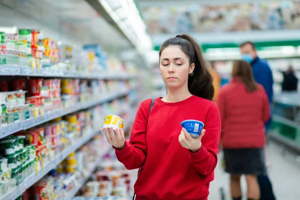 Egy Fiatal Kaukázusi Áll Egy Szupermarketben Megfontoltan Választ Két Joghurt — Stock Fotó