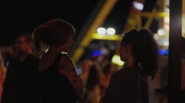 Lunaparktaki gece hayatı. Birbiriyle konuşan iki genç kadın. Arka planda neon ışıkları olan ışıltılı bir çekim. Karnaval ve tatil.