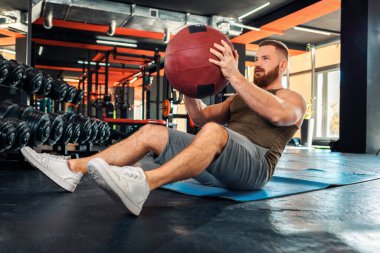 Spor salonunda ilaç topuyla antrenman yapan sakallı genç bir sporcu. Düşük açı. Zindelik kavramı.
