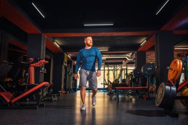 Genç kaslı atletik bir adam spor salonunda yürüyor. Düşük açı. Spor ve spor konsepti.