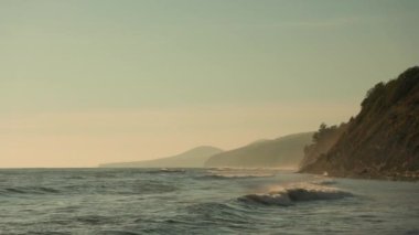 Vahşi bir sahil yakınında köpüklü fırtına dalgaları. Güneşli bir hava. Yavaş çekim.