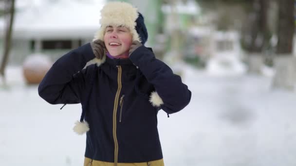 若い女性が笑顔で帽子を調整し 紐を結びつけています 背景には雪に覆われた通り スローモーション — ストック動画