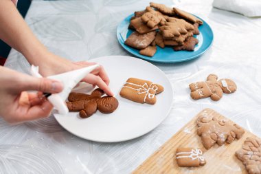 Bir dişinin elleri zencefilli ekmeği krema şekeriyle süslüyor. Tabaktaki kurabiyelerin yakın çekimi. Noel yemeği konsepti ev yapımı yemekler.