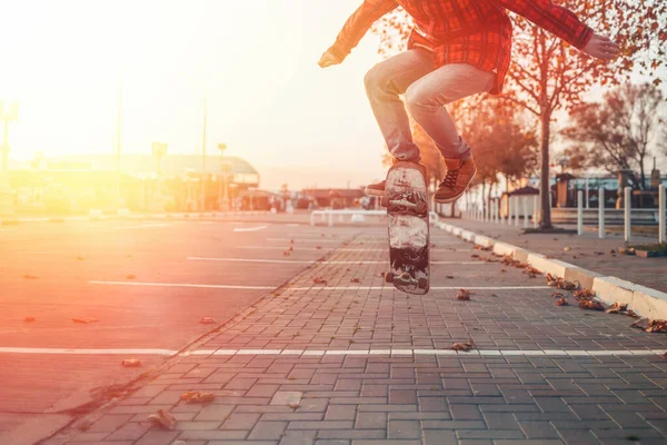 Skateboarding. A man does an Ollie stunt on a skateboard. Jump in the air. Close-up of legs. Sunlight.