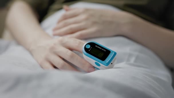 人差し指のパルス酸素濃度計を使ってベッドに寝そべっている女性 手を閉じる リアルタイムだ 血液中の酸素の決定の概念 — ストック動画