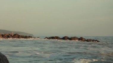 Açık havada fırtınalı deniz ya da okyanus manzarası. Büyük köpüklü dalgalar kayalara çarpıyor. Yavaş çekim.