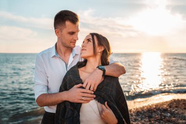 Yeni evlilerin balayı. Bir erkek kadınını kucaklar. Arka planda deniz ve günbatımı. Sevgililer Günü Konsepti.