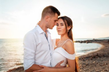 Düğün günü. Yeni evliler kucaklaşıp sahilde poz verirler. Arka planda, gün batımı ve okyanus. Sadece neşeli konsept..