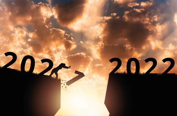 New Year 2022. Silhouette of a person pushing number one in abyss. Dramatic sunset is on the background. Concept of changing the calendar year.