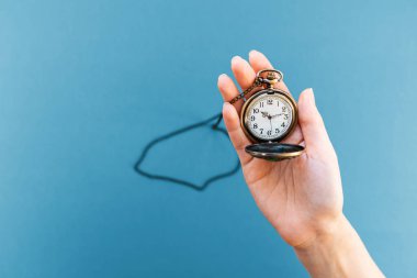 Kadının eli klasik bir saati tutuyor. Mavi arka plan. Düz yatıyordu. Uzayı kopyala Zaman yönetimi kavramı.