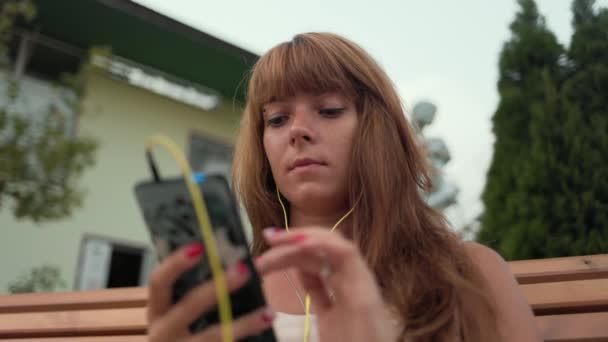 Młoda Kobieta Słuchawkami Siedząca Ławce Używająca Telefonu Rękach Zamknij Portret — Wideo stockowe