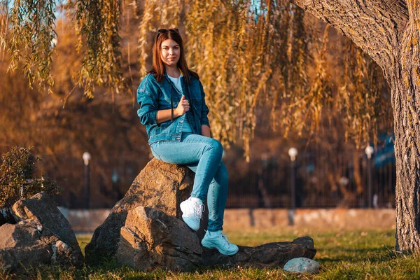 若いきれいな女性が秋の公園の岩の上に座っている 心理学の概念 — ストック写真