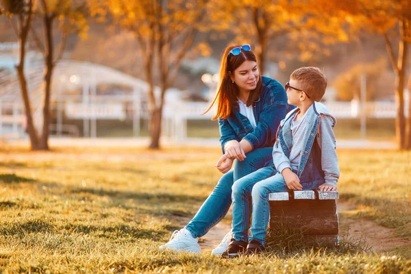 秋天的季节一位年轻的母亲和她的儿子一起坐在公园的长椅上 幸福童年的概念 — 图库照片