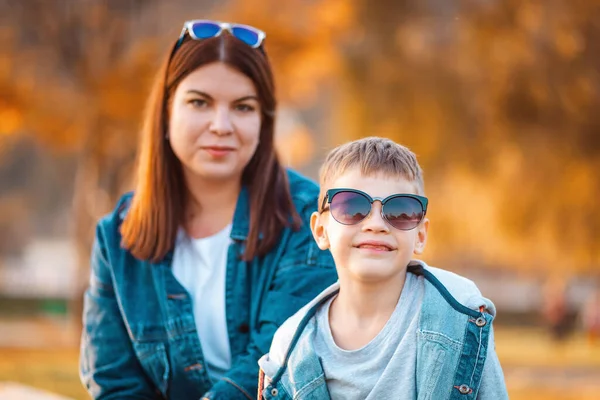年轻微笑的母亲和她的儿子的画像 背景是秋天的公园 幸福童年的概念 — 图库照片